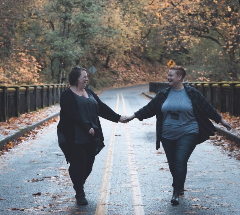 Couple holds hands while walking down the middle of a road, surrounded by fall foliage