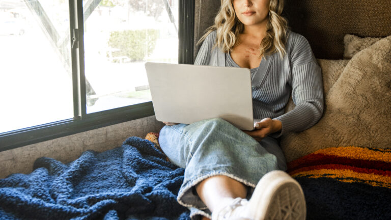 woman sitting on bed in an rv with her laptop