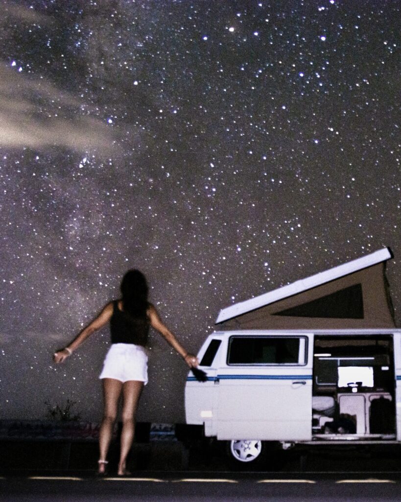 a woman by a campervan at night with lots of stars