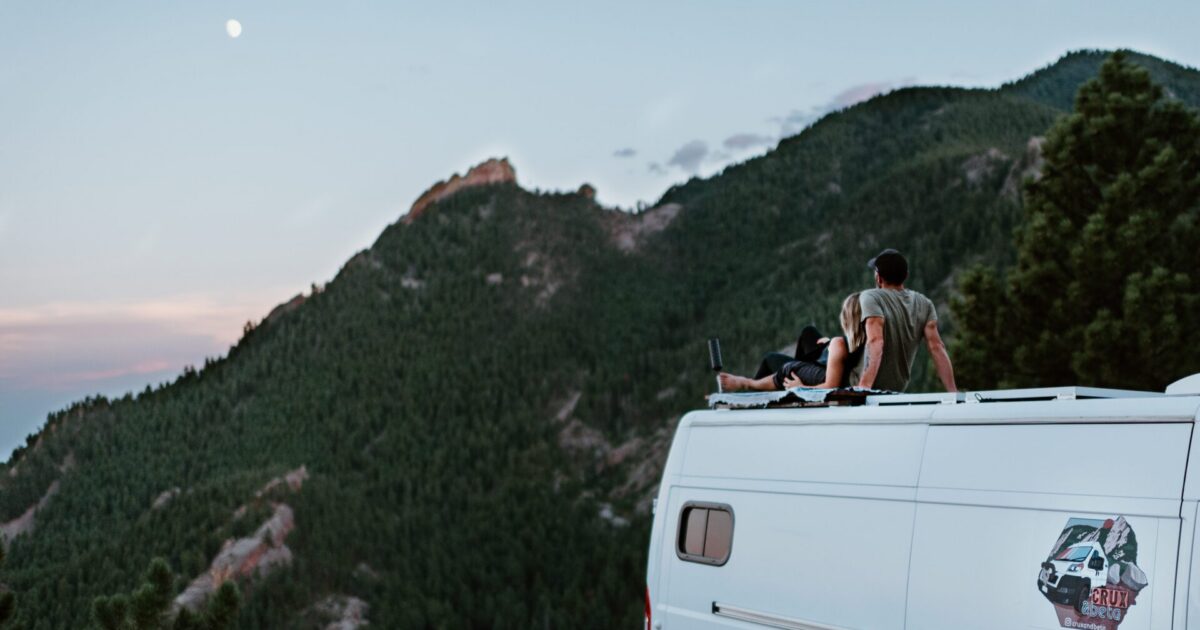 a couple on the rooftop of a van watching the moon and mountain environment