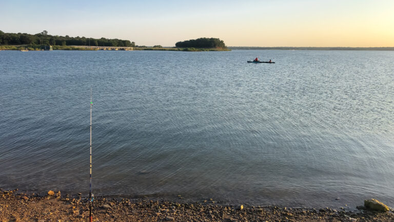 Bank fishing with fishing pole on rod holder and people on kayak at the distance on on Grapevine Lake, North Texas, America