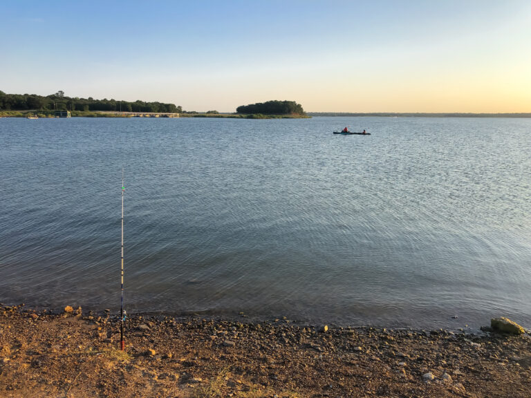Bank fishing with fishing pole on rod holder and people on kayak at the distance on on Grapevine Lake, North Texas, America