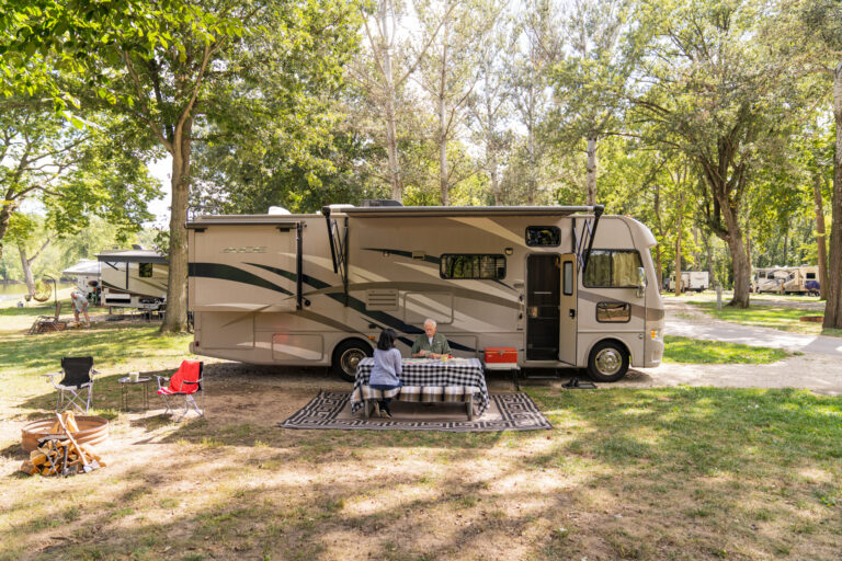 senior couple at a picnic table in front of a Class A RV delivered to a campsite