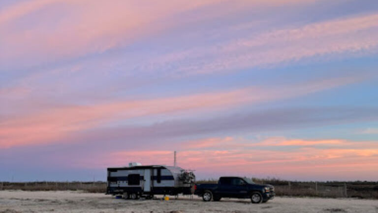RV travel trailer parked on the beach at sunset