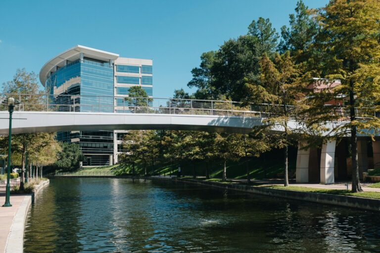 Modern glass building with a pedestrian bridge over the Woodlands Waterway.