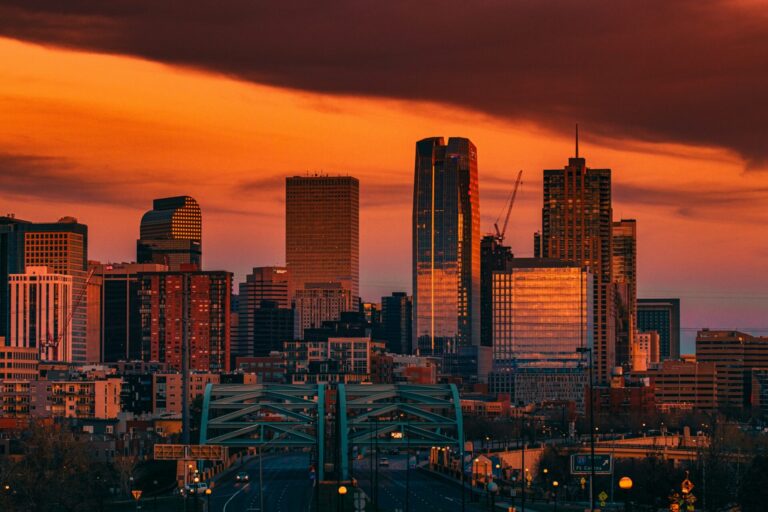 An orange sunset illuminates skyscrapers above city streets in Denver, CO.