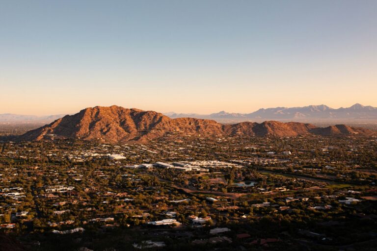 Aerial vista of a tree-lined city with foothills and a mountain range background.