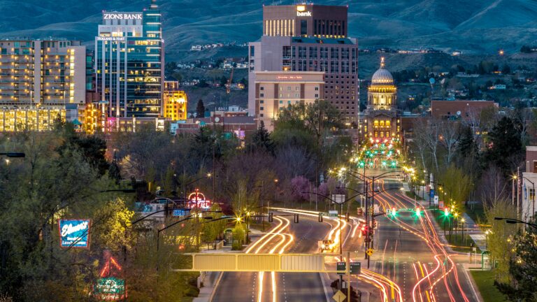 Downtown buildings lit up at night with mountains in the background