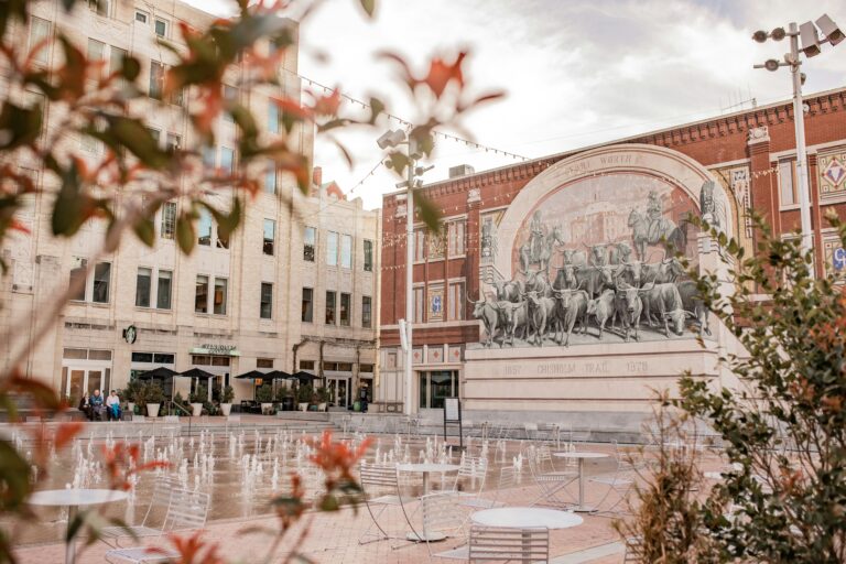 A building with a mural of cattle behind an open area with tables and chairs and several small fountains.