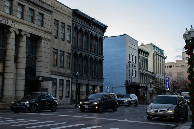 Historic downtown street with old bank building, varied architecture, and cars on road at dusk.