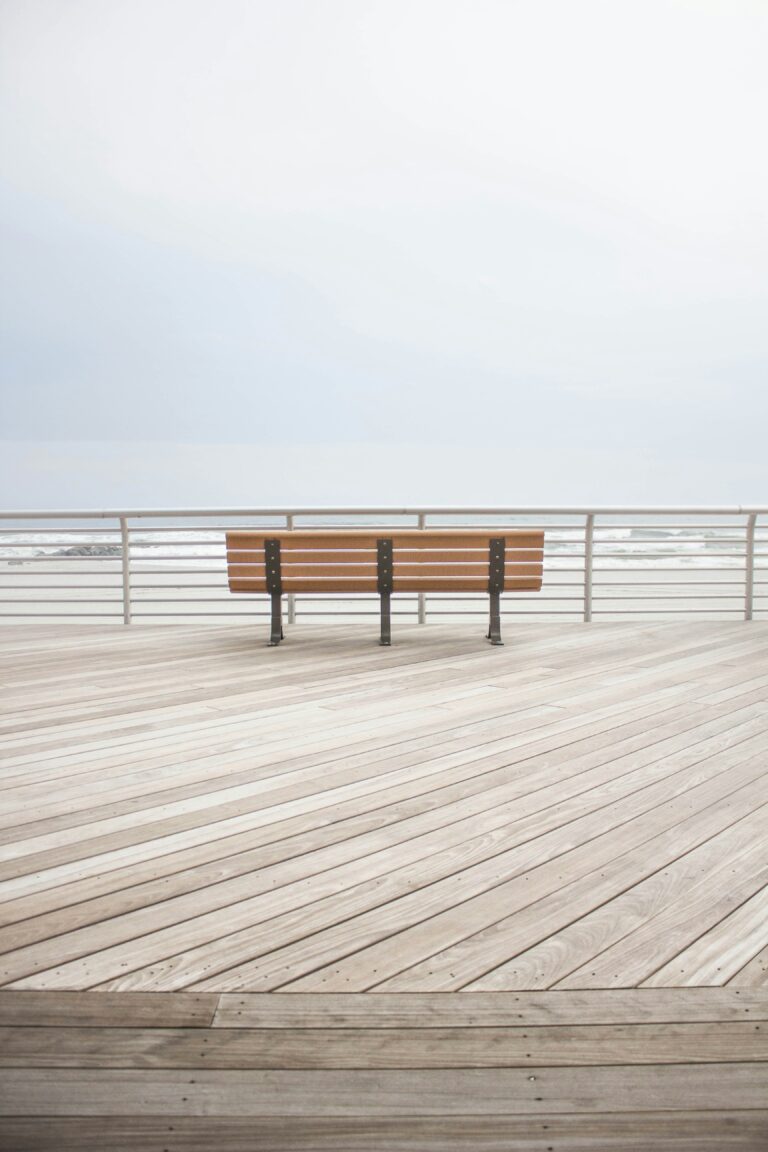 A brown wooden bench at the dock in front of the ocean on a cloudy day