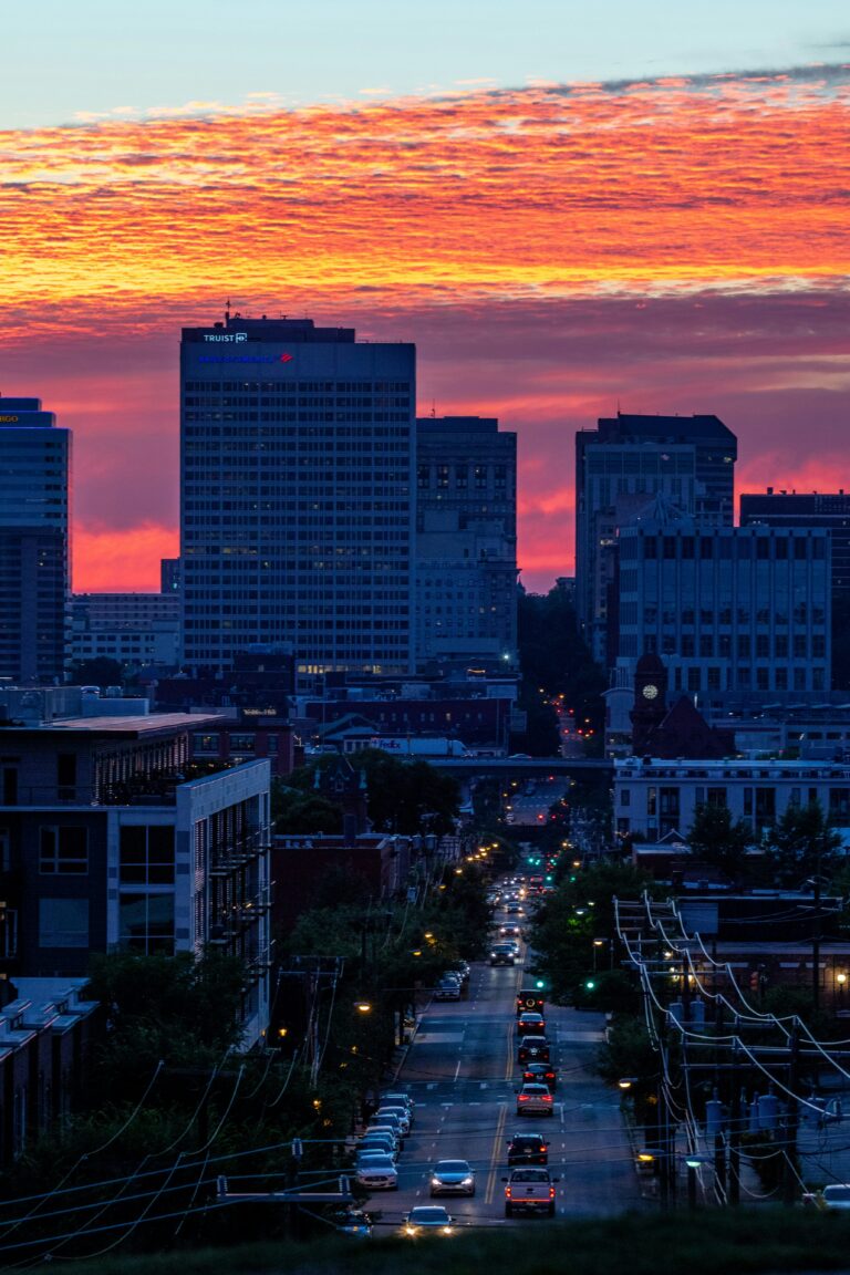 Richmond skyline at sunset with vibrant orange sky, tall buildings silhouetted, and a busy street leading into downtown.