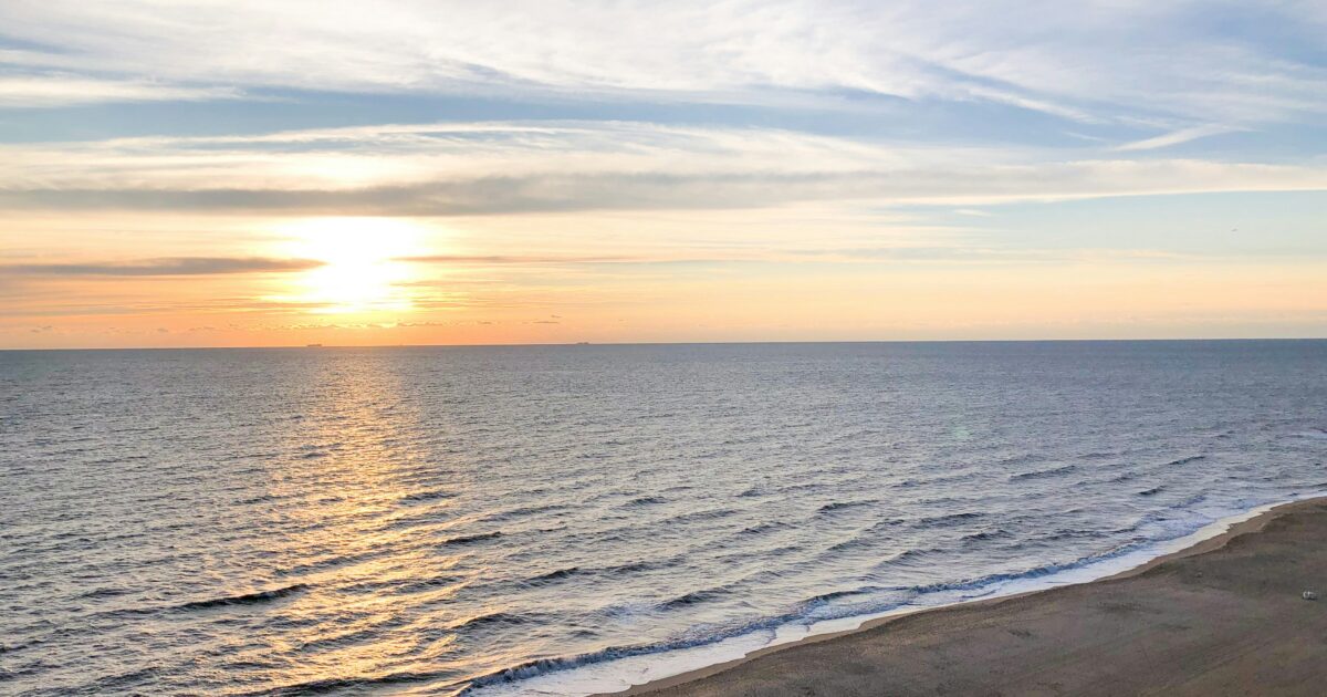 The sun sinks on the horizon as waves crash into the sand at Virginia Beach.