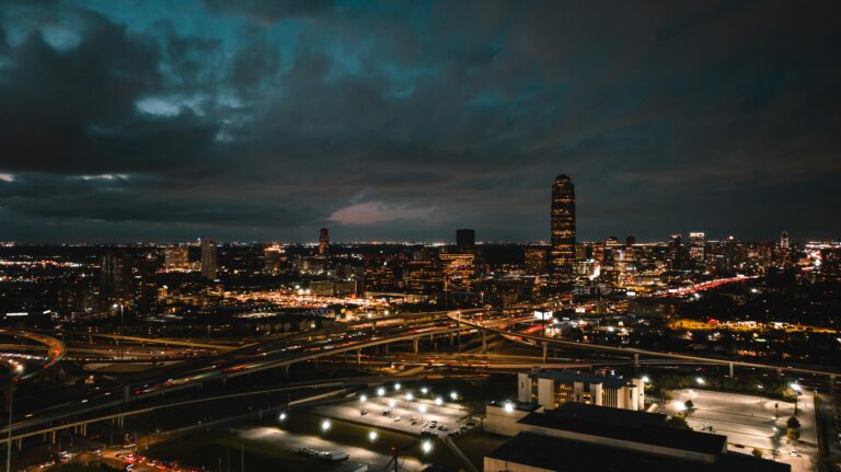 A drone's-eye view of the city at night with lights aglow against a dark, cloudy sky