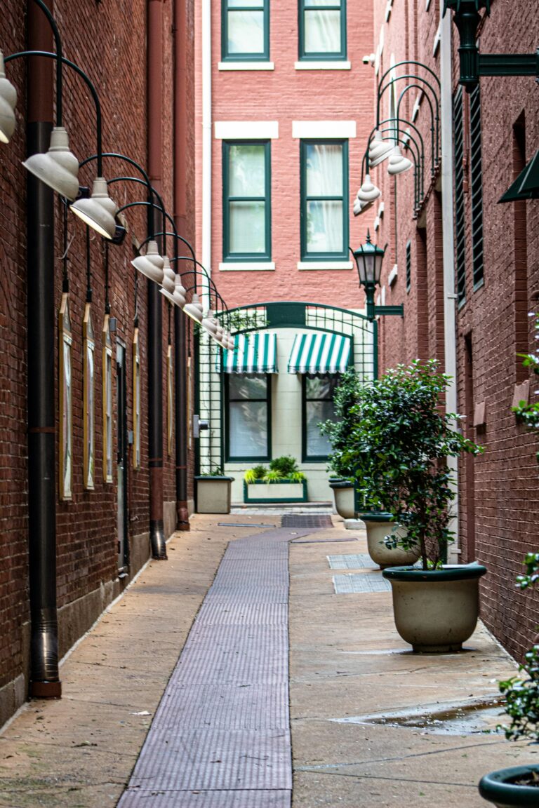 Narrow brick alley in Memphis with arched lamps, potted plants, and a striped awning visible at the end.