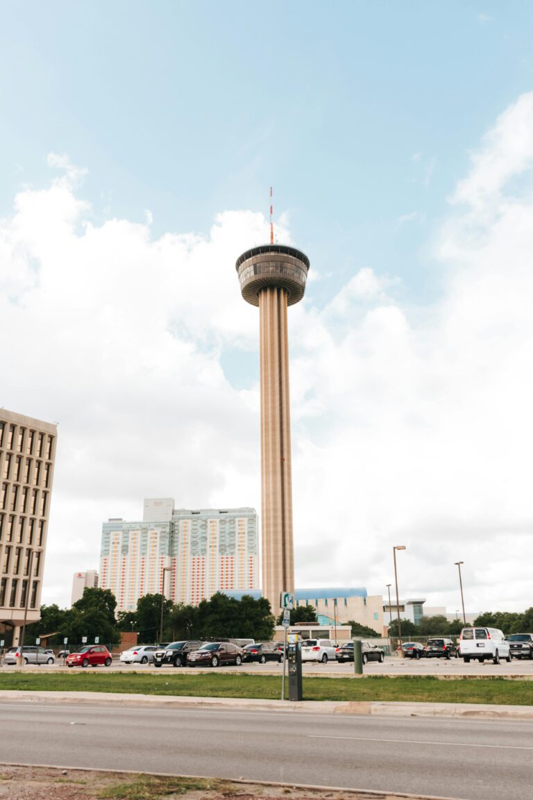 The 750-foot-tall Tower of the Americas stands out amid several high-rise buildings under a cloudy sky.