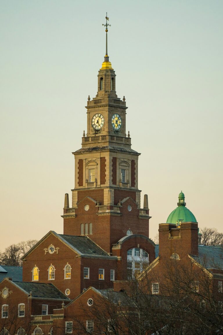 A tall clock tower rises above a historic brick building in Providence, RI, with a green domed roof visible in the background.