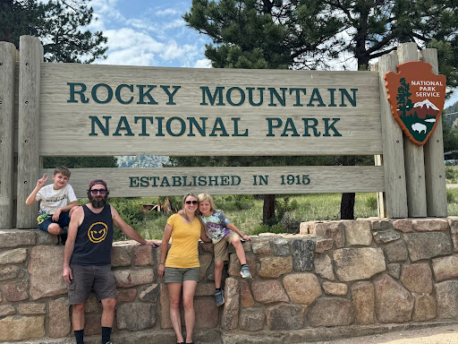 family with kids next to rocky mountain national park entrance sign