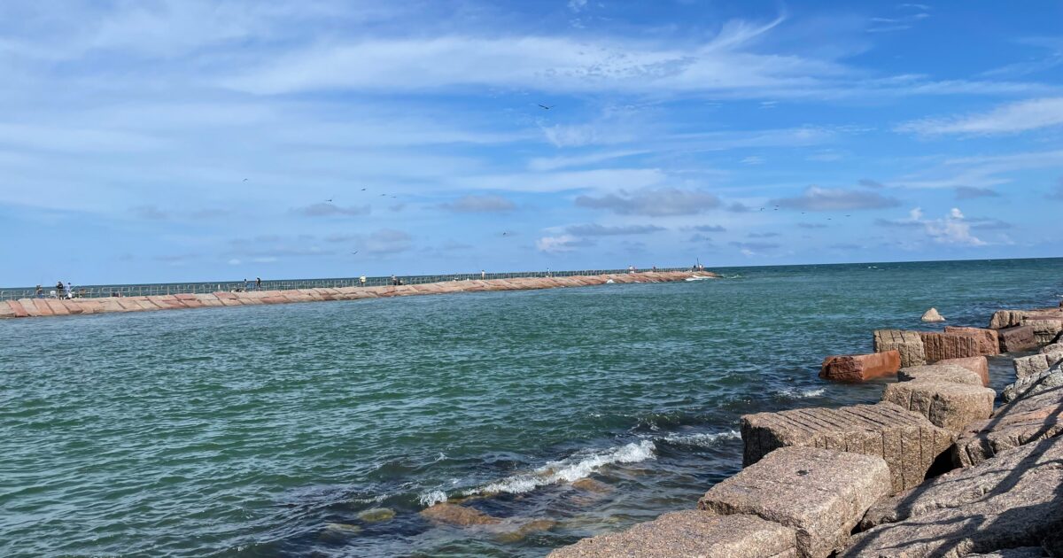 The blue-green water of Packery Channel sits under a blue sky with wispy clouds