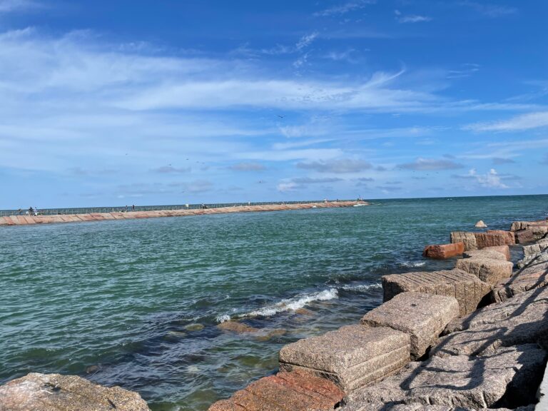 The blue-green water of Packery Channel sits under a blue sky with wispy clouds