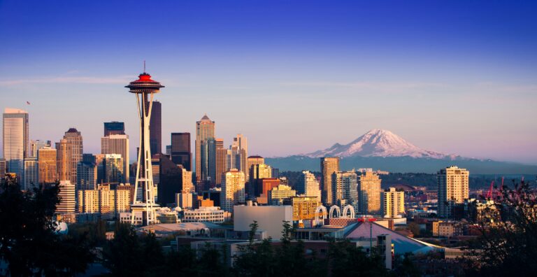 Sun-dappled buildings of various sizes and shapes, a white tower with a red, circular top, and a snow-capped mountain.