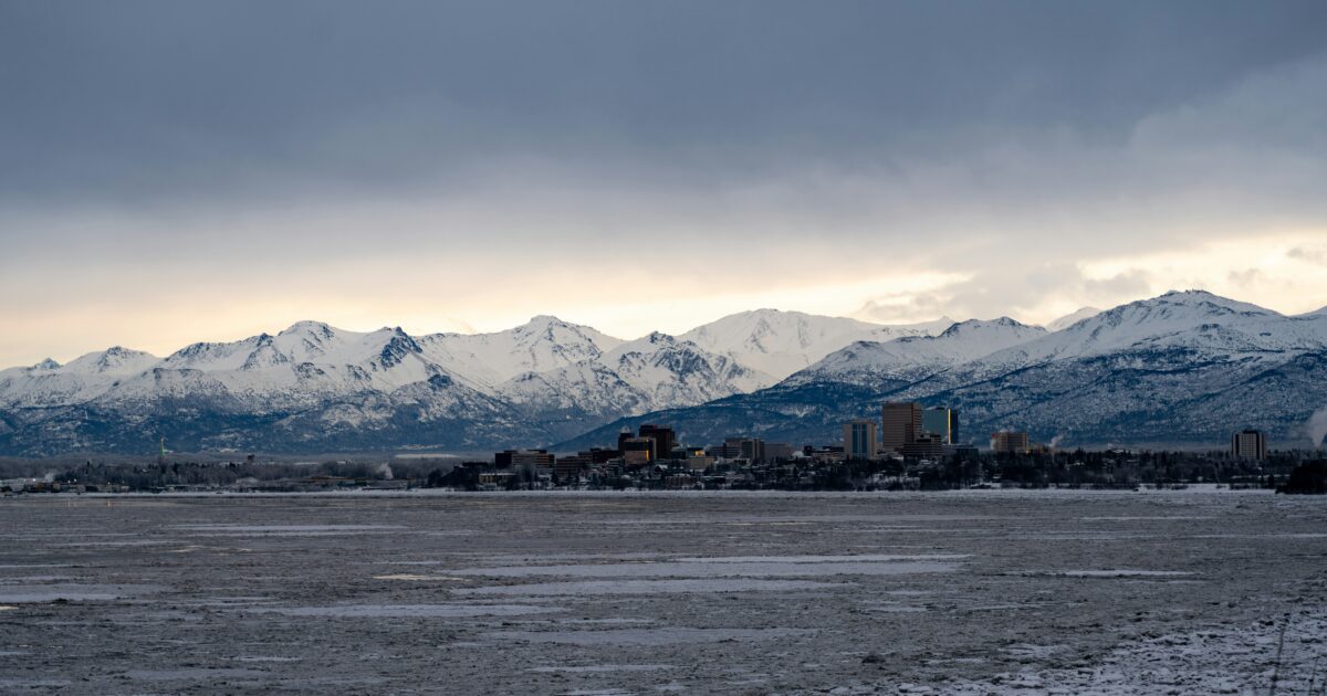 A landscape view of the Anchorage city skyline with snow-covered mountains in the background.