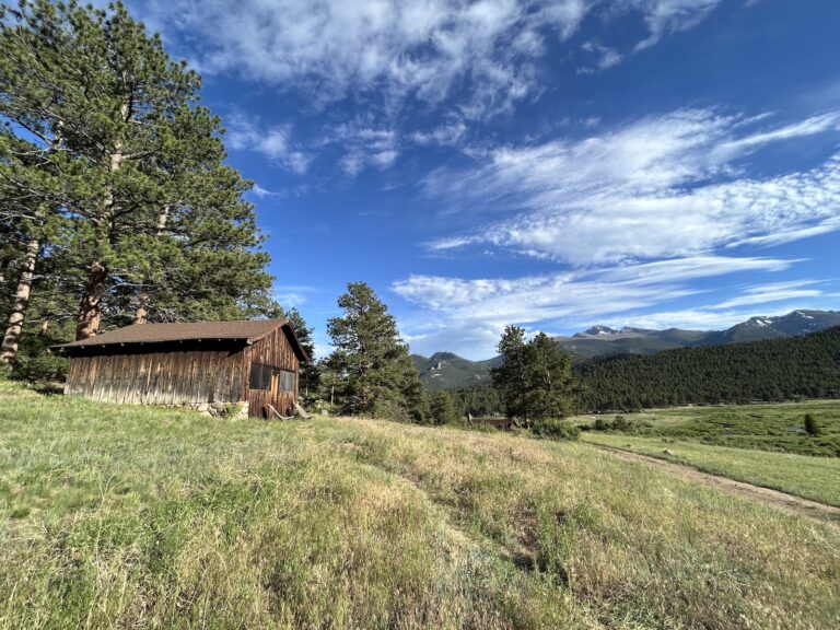 View of an old cabin with mountains and clouds in the background.