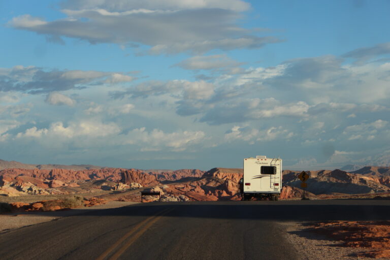 RV driving down a desert road surrounded by red rocks