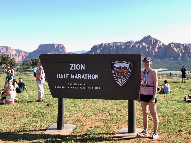 woman in race gear standing in front of a sign that says 'zion half marathons'