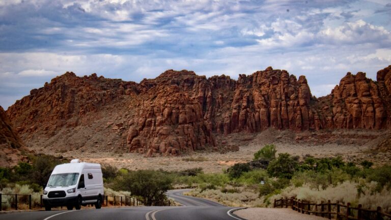 A campervan parked on the shoulder of a road with gnarled rocks in the background and clouds overhead.