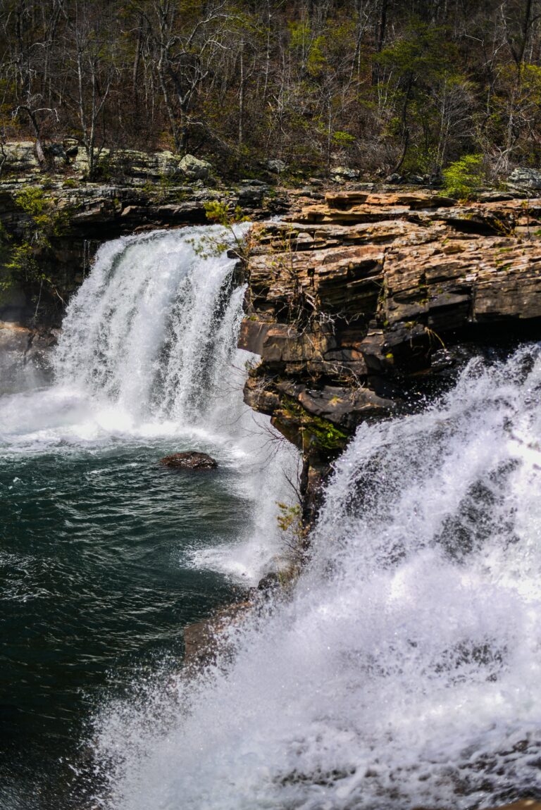 Cascading waterfall between large boulders surrounded by trees.