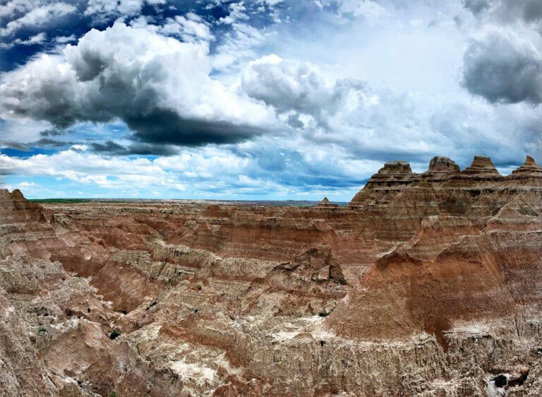 Rugged red rocks rise up to meet a blue sky full of dark, puffy clouds