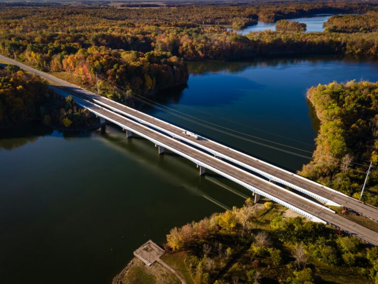 An aerial view of a double bridge crossing over a winding river surrounded by lush greenery.