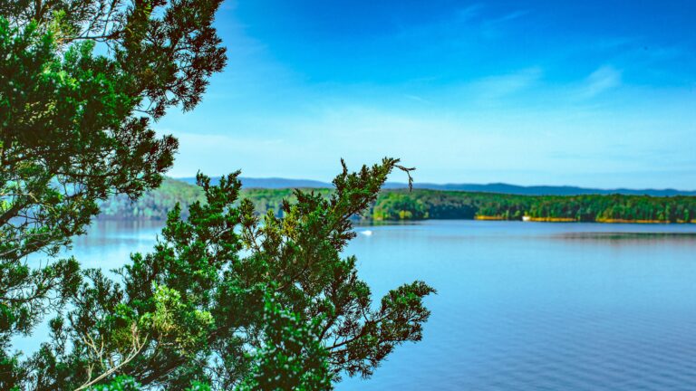 Glimmering blue lake under a mostly sunny sky with green hills in the background.