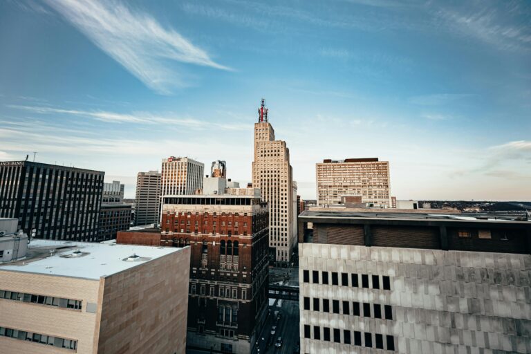 Tan, gray, and brown buildings in a city under a blue sky with wispy clouds.