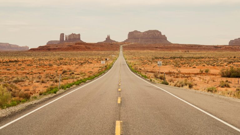 Long desert highway stretches toward the towering red buttes of Monument Valley.