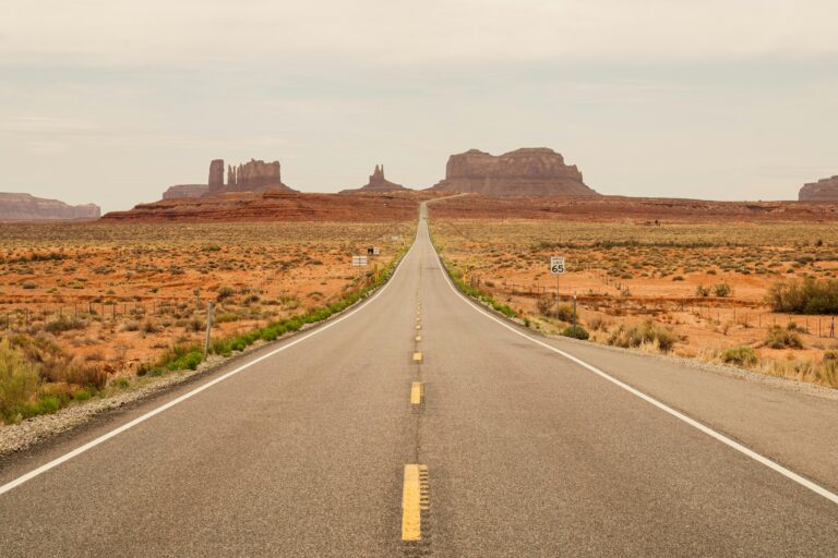 Long desert highway stretches toward the towering red buttes of Monument Valley.