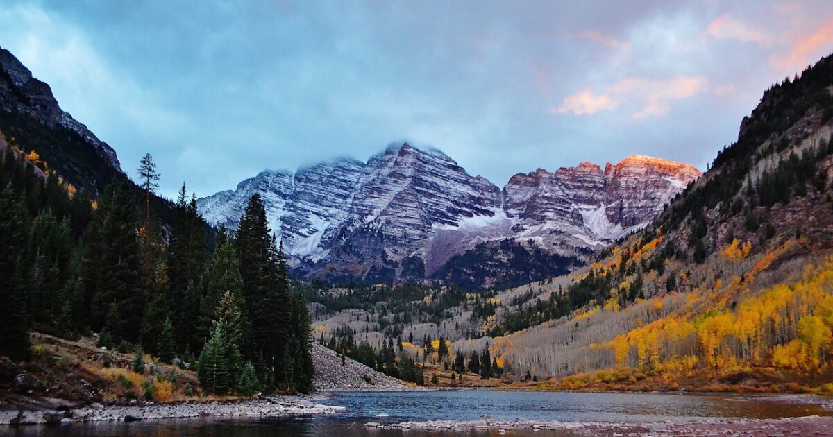 A view of the Rocky Mountains with fall foliage and a placid lake in front
