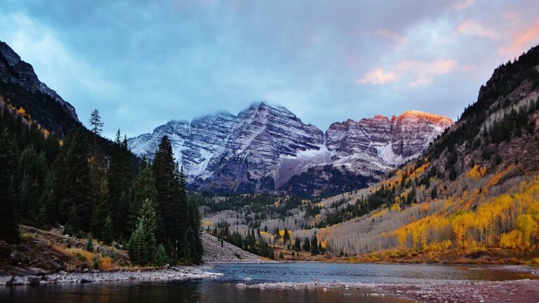 A view of the Rocky Mountains with fall foliage and a placid lake in front