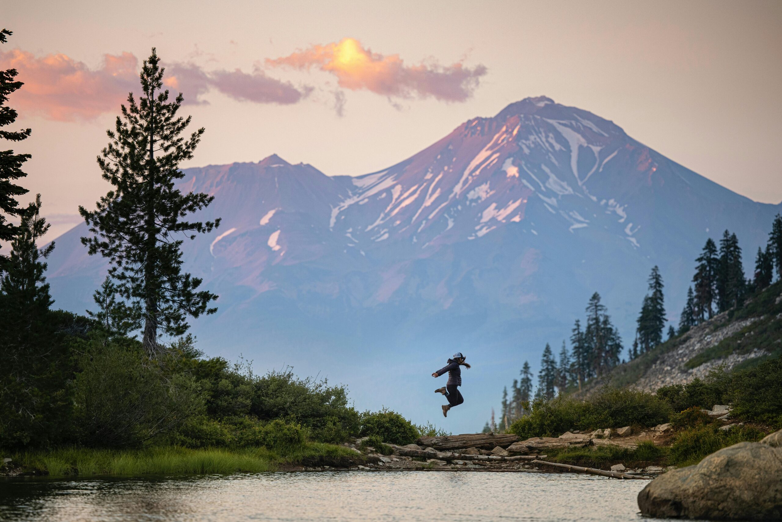 a person jumping in front of mountains in the mount shasta national forest with a bucket list view