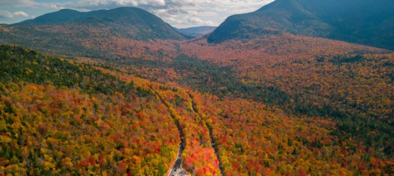 An aerial shot of the Kancamagus highway with bright colored fall foliage and mountains in the background. Kancamagus Highway RV travel is a great way to see fall colors