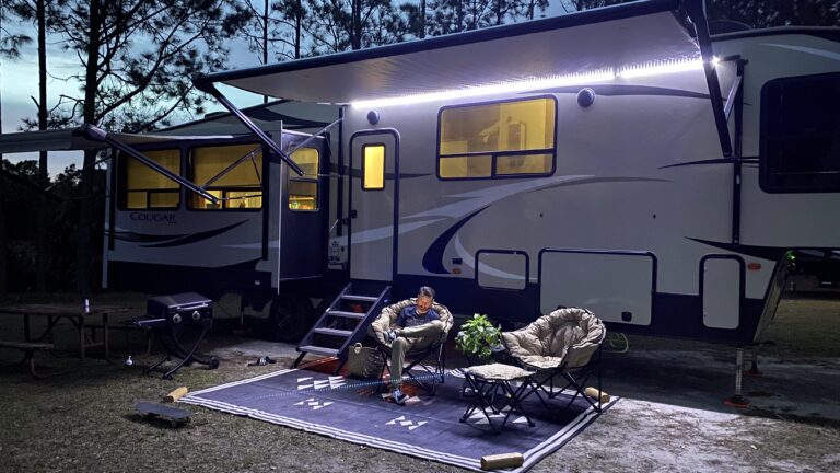 A man relaxes outside of his RV under a lit canopy
