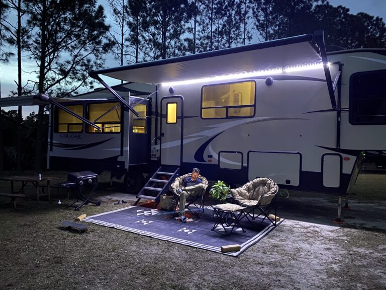 A man relaxes outside of his RV under a lit canopy