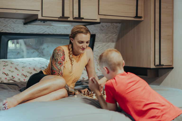 A woman and her son play chess inside their motorhome's master bedroom