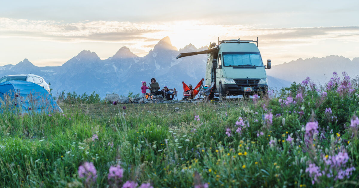 A family with kids next to an RV in front of a mountain range