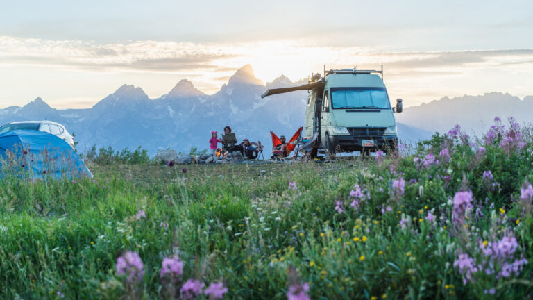 A family with kids next to an RV in front of a mountain range