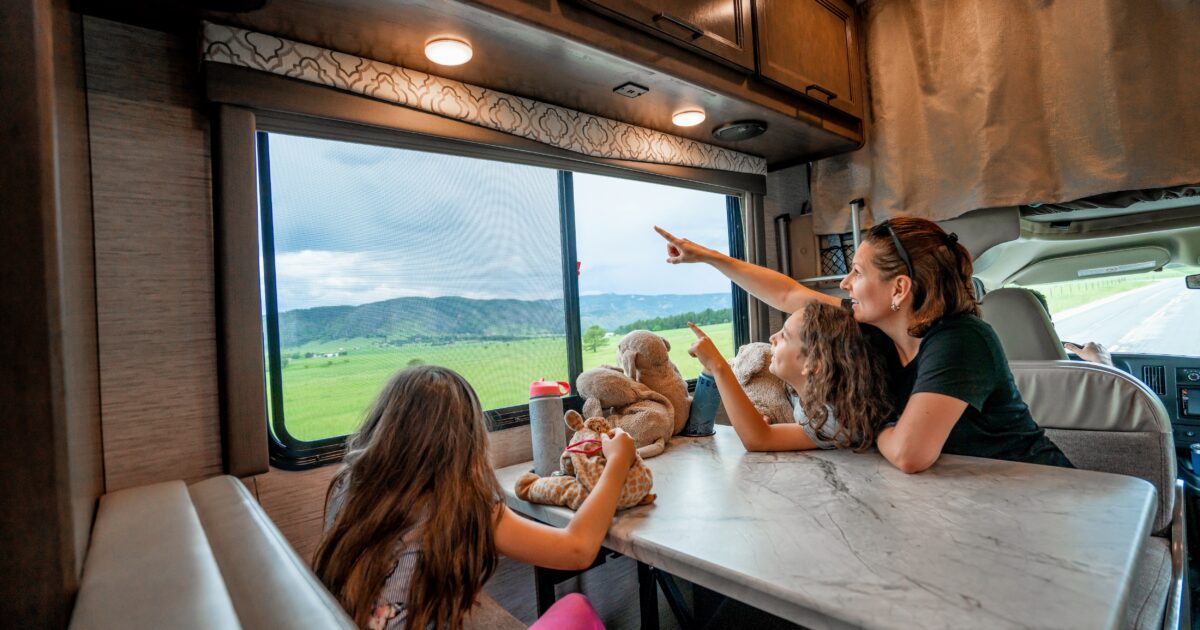 A family looks out the window at a storm over green rolling hills from an RV dinette set