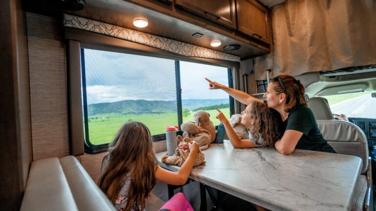 A family looks out the window at a storm over green rolling hills from an RV dinette set
