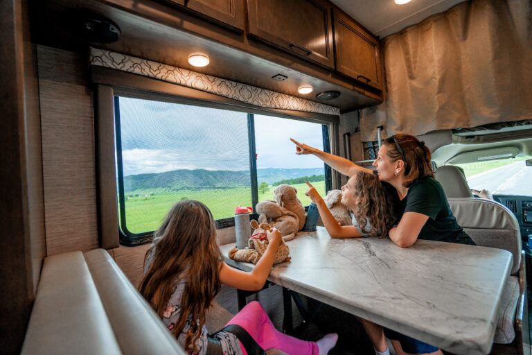 A family looks out the window at a storm over green rolling hills from an RV dinette set