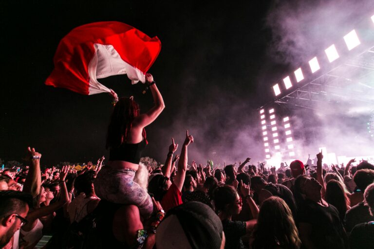A young woman sits atop her companion's shoulders, cheering at a nightime show at a music festival
